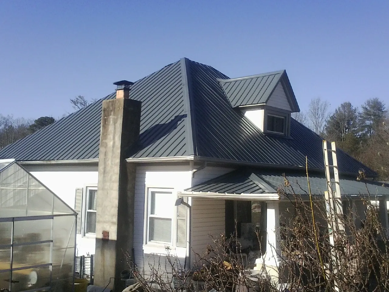 Dark blue standing seam metal roof on a white farmhouse with dormer — Slate & Tile Roof Repair by Roofing Brothers in Bernardsville