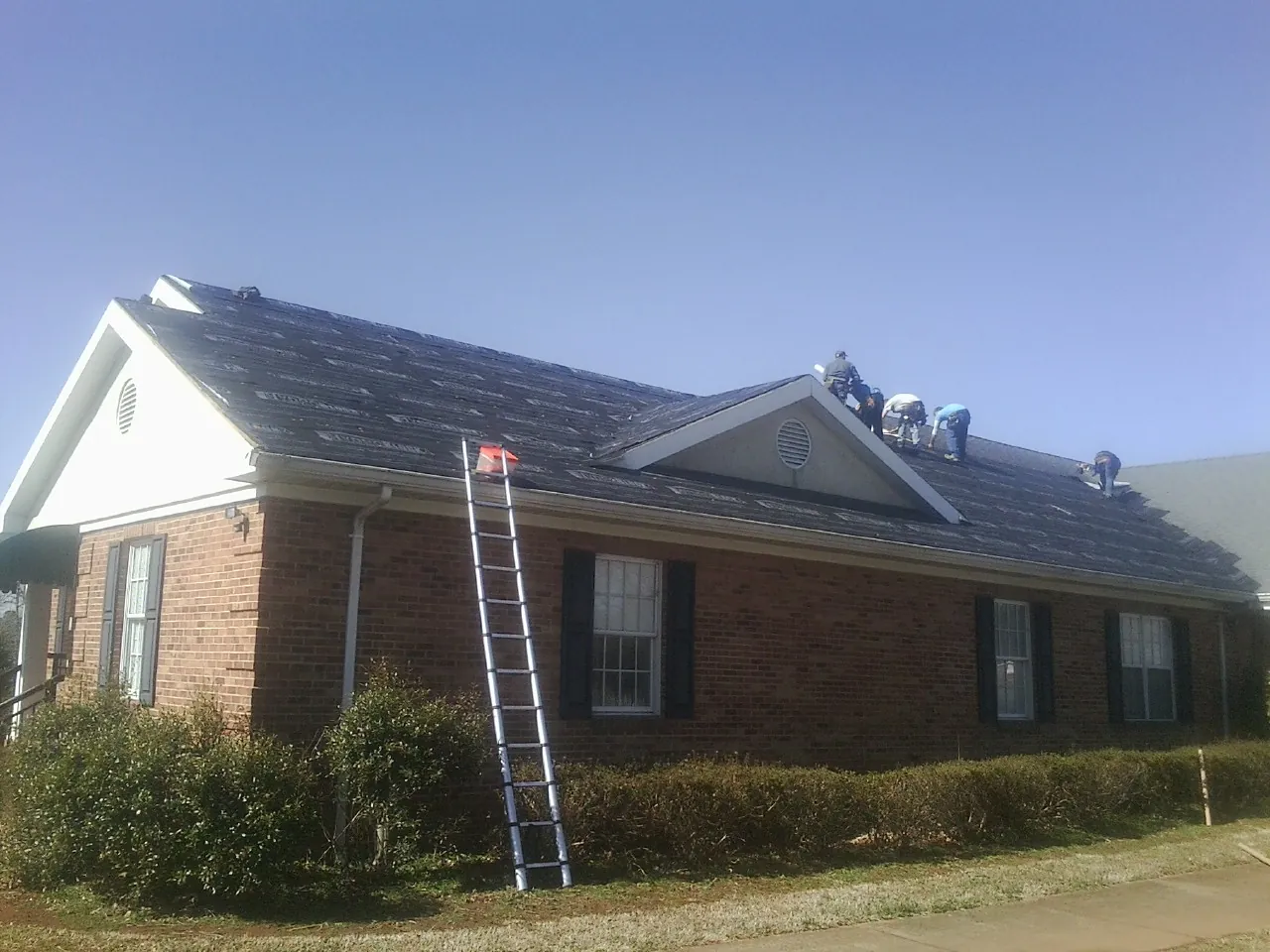 Crew tearing shingles off a brick ranch roof with a ladder set — Emergency Roof Repair work by our crew in Bernardsville