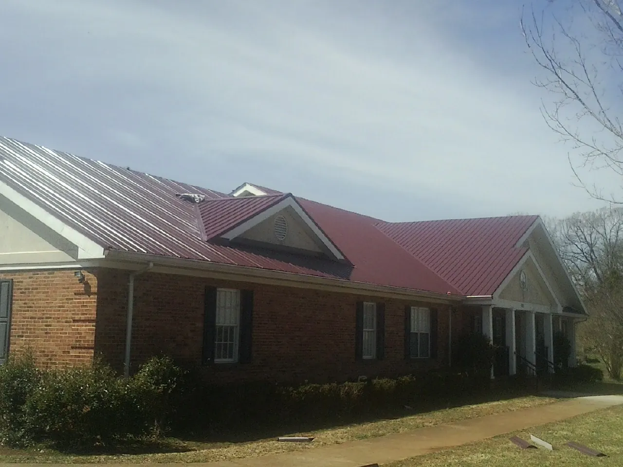 Red metal roof with gabled entries on a long brick building, from a Hail Damage Roof Repair job in Bernardsville