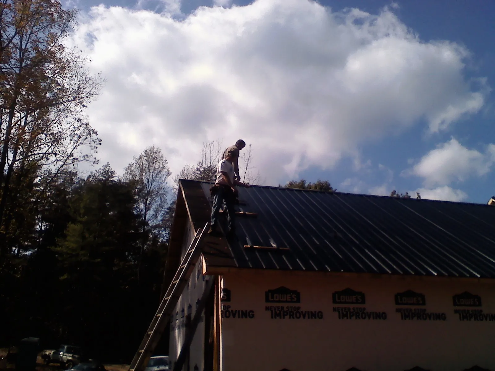 Roofer fastening dark metal panels high against a cloudy sky, from a Roof Inspection job in Bernardsville