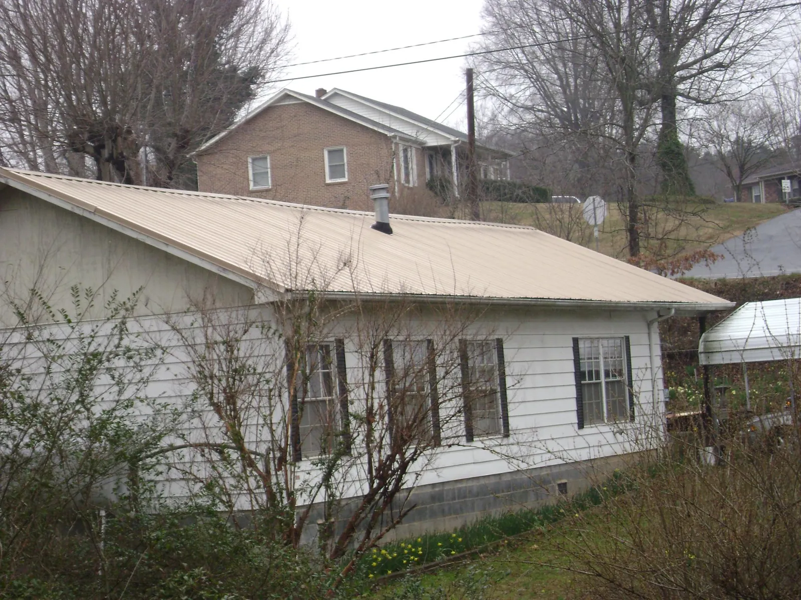 Tan metal roof on a white sided house set into a hillside — Commercial Roofing by Roofing Brothers in Bernardsville